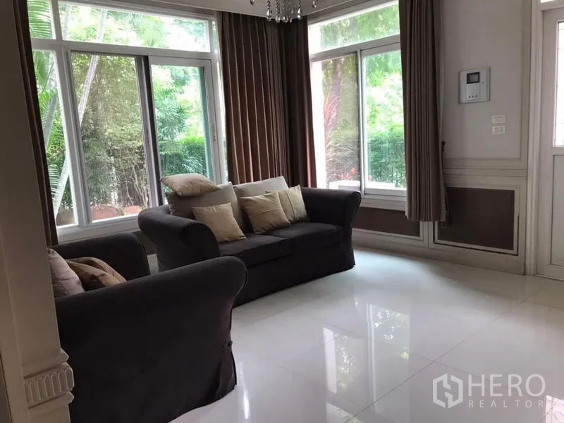 Detached House for rent in Bang Khen, Bangkok - Living room with sofas, large windows, curtains and garden views.