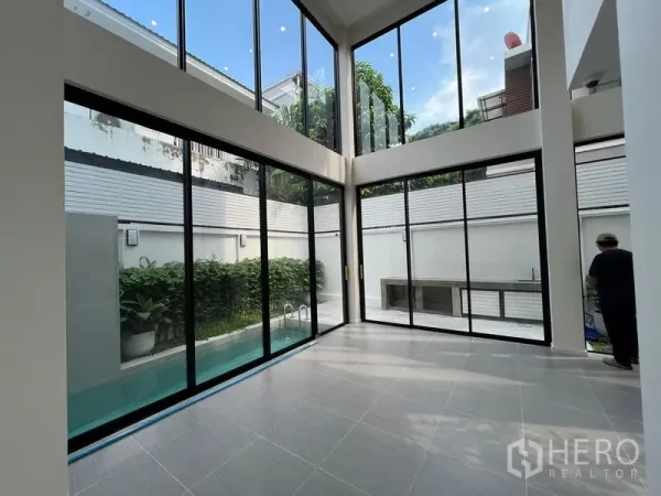 Home Office for sale in Phra Khanong, Bangkok - Double‑height living area with floor‑to‑ceiling windows opening to a courtyard and slim private pool.
