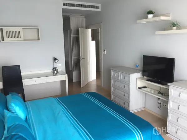 Condominium for rent in Bangkok - Cozy bedroom with blue bedding, work desk, drawers, wall shelves and a flat-screen TV.