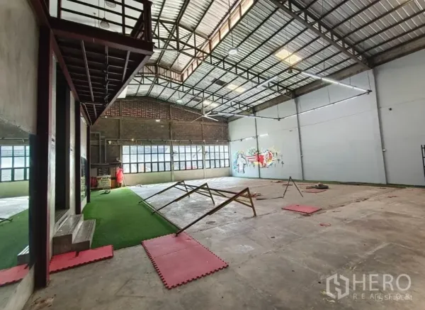 Warehouse for rent in Khlong Toei, Bangkok - Wide shot of a high-ceiling warehouse with steel trusses, a turf lane and large windows.