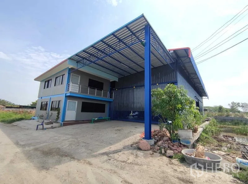 Warehouse for sale in Nakhon Pathom - Front elevation of the warehouse featuring tall blue columns, large canopy and ample loading/parking space.