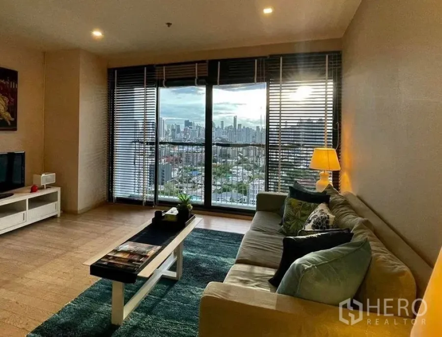 Condominium for rent in Watthana, Bangkok - Bright living room with sofa, TV console, and panoramic skyline through full-height glass doors.