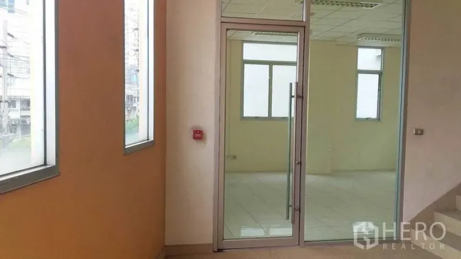 Office Space for rent in Phra Khanong, Bangkok - Building corridor with a glass door leading into a bright office unit.