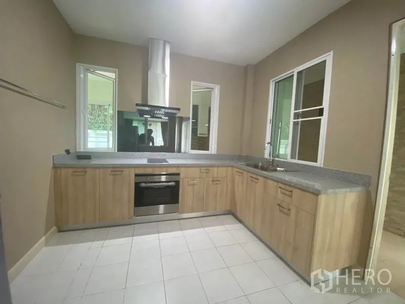 Detached House for rent in Prawet, Bangkok - U-shaped modern kitchen with wood cabinets, built-in oven, cooktop and range hood.