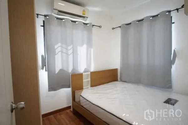 Townhouse for rent in Suan Luang, Bangkok - Compact bedroom with double bed, air conditioner and gray curtains on wood flooring.