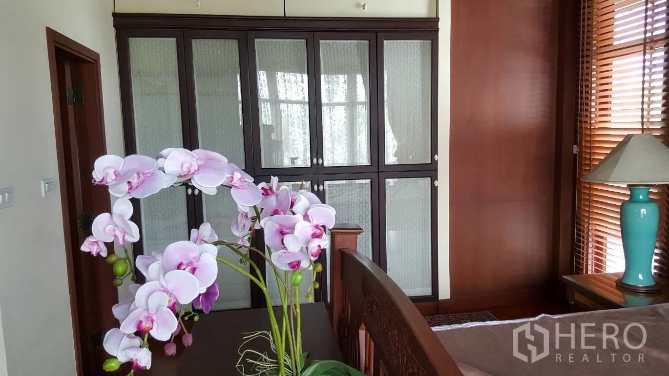 Detached House for rent in Khlong Toei, Bangkok - Bedroom with built-in glass-door wardrobe, wooden blinds and an orchid arrangement on a table.