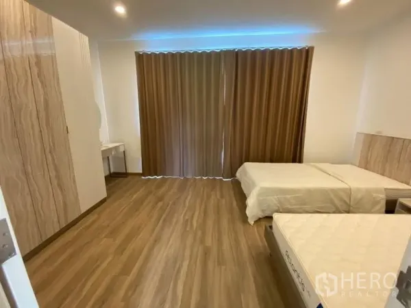 Townhouse for rent in Bang Kapi, Bangkok - Guest bedroom with twin beds, wood floors, full-length curtains, and built-in wardrobe.