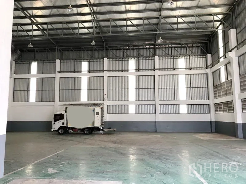 Factory for rent or sale in Samut Prakan - Open warehouse floor with truck access beneath bright roof panels for natural light.