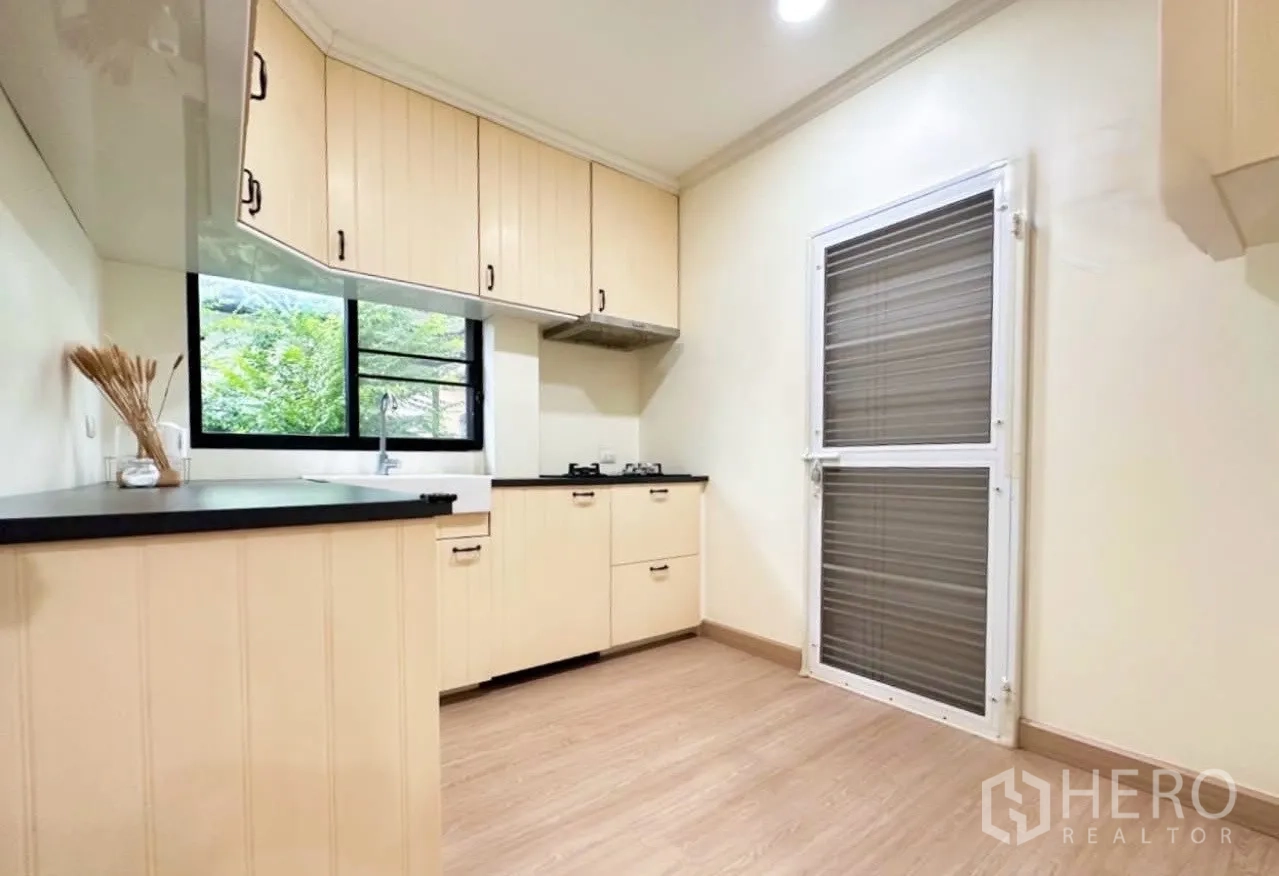 Detached House for sale in Lam Luk Ka, Pathum Thani - Kitchen view with back door, upper cabinets, sink by the window and ample floor space.