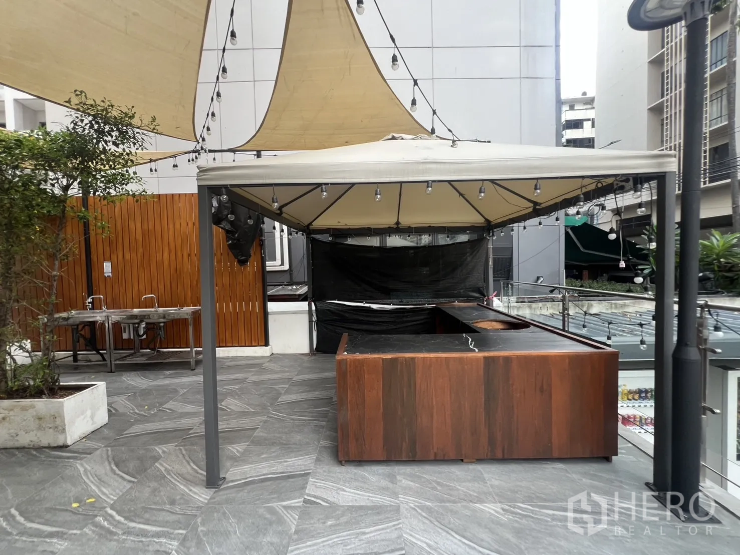 Retail Space for rent - Outdoor kiosk bar under canopy sail with string lights on a tiled plaza.
