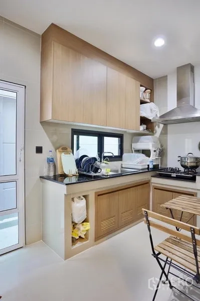 Detached House for rent or sale in Bang Kapi, Bangkok - Compact Thai kitchen with gas hob, stainless hood, stone countertop and light wood cabinetry.