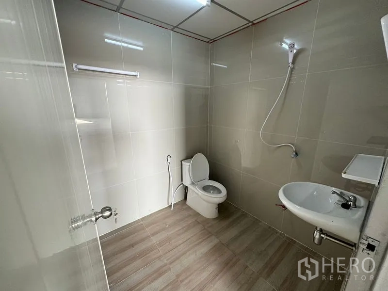 Warehouse for rent in Lam Luk Ka, Pathum Thani - Clean tiled bathroom with toilet, sink and shower inside the warehouse.