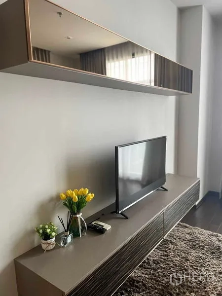 Condominium for rent or sale in Watthana, Bangkok - Living room with black leather sofa, glass coffee table and wood-paneled feature wall.