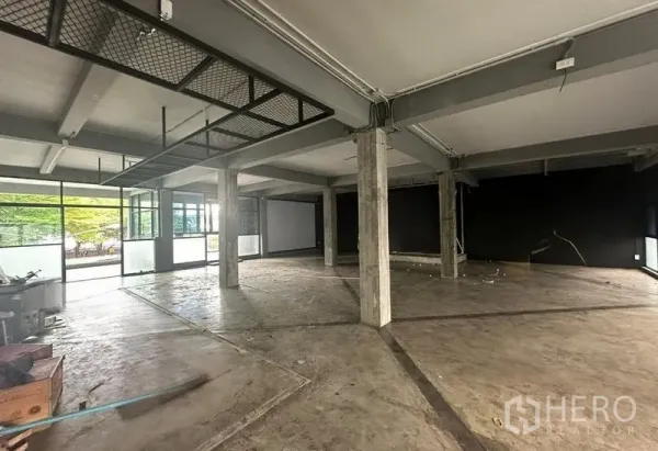 Retail Space for rent - Open-plan retail interior with concrete floor, exposed columns and full-height glass facing a green plaza.