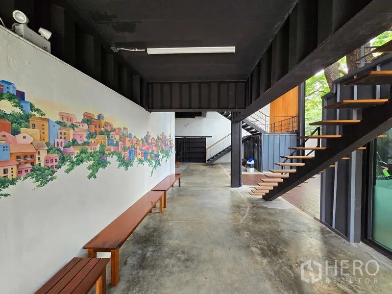 Home Office for rent in Chatuchak, Bangkok - Covered corridor with a colorful mural, wooden benches, and steel stairs on polished concrete.