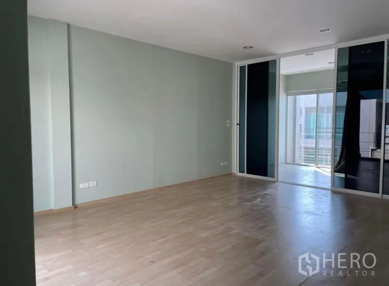 Townhouse for rent in Suan Luang, Bangkok - Spacious multipurpose room featuring wood floors and a glass partition leading to a balcony.