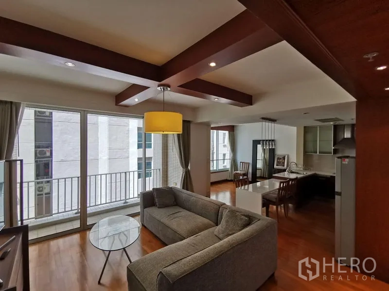 Condominium for rent in Pathum Wan, Bangkok - Bright living area with ceiling beams, balcony doors, and city-facing windows.