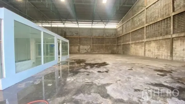 Warehouse for rent in Prawet, Bangkok - Warehouse corner showing a glass-enclosed office unit, polished concrete floor and metal truss roof with bright lighting.
