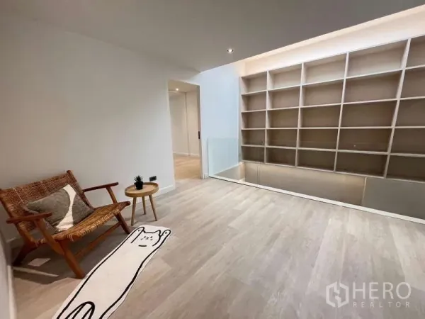Townhouse for sale in Khlong Toei, Bangkok - Bright upstairs landing with built-in shelving wall, wicker chair and light wood flooring.