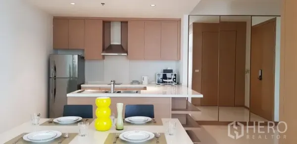 Condominium for rent in Khlong Toei, Bangkok - Contemporary kitchen with island counter, cooktop and mirrored storage wall.