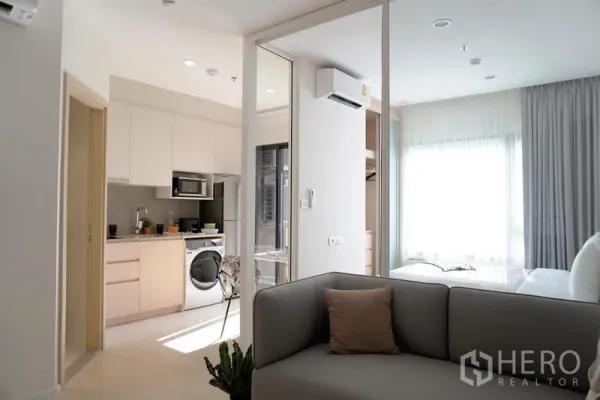 Condominium for rent in Pathum Wan, Bangkok - Modern kitchen with built-in cabinets and washer beside a glass door to the bright bedroom.