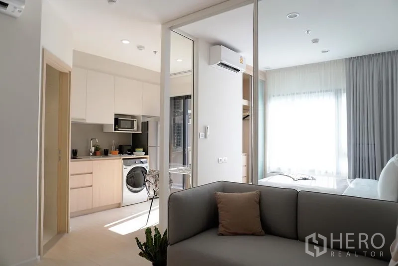 Condominium for rent in Pathum Wan, Bangkok - Modern kitchen with built-in cabinets and washer beside a glass door to the bright bedroom.