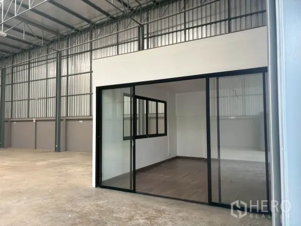 Warehouse for rent in Mueang Pathum Thani, Pathum Thani - Warehouse interior with a glass-partitioned office and polished concrete floor beneath a high steel roof.