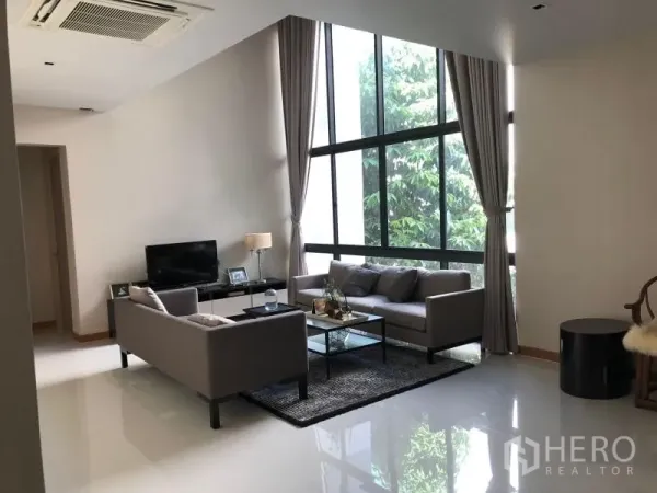 Detached House for rent or sale in Huai Khwang, Bangkok - Bright lounge with large glazing, two sofas, TV unit, tall curtains and glossy floors.