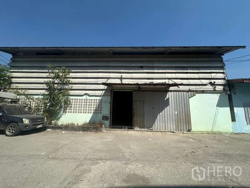 货栈 出租在Suan Luang, Bangkok - 仓库正立面，金属滑门，前方有混凝土装卸区。
