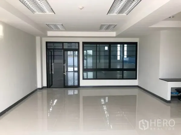 工厂 出租在Samut Prakan - 明亮瓷砖办公区，玻璃门与黑框窗户，可眺望厂房内部。