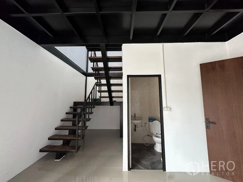 Warehouse for rent in Lam Luk Ka, Pathum Thani - Ground-floor office corner with open-riser staircase to mezzanine and a tiled restroom.