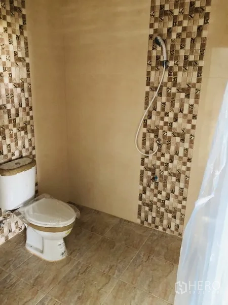 Warehouse for rent in Bang Kapi, Bangkok - Clean tiled restroom with toilet and handheld shower inside the warehouse.