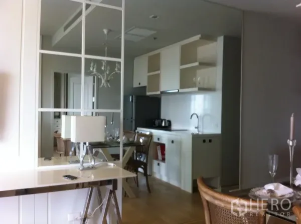 Condominium for rent in Bangkok - Kitchen with mirror partition, glass dining table, and white cabinetry.