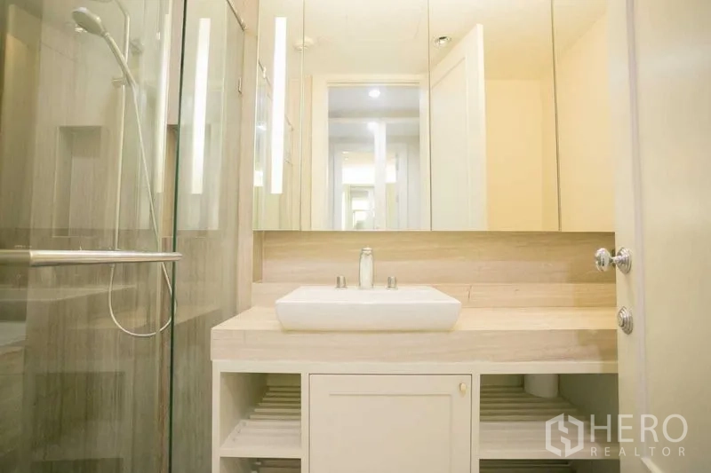 Condominium for rent or sale in Pathum Wan, Bangkok - Contemporary bathroom with glass shower, wide vanity and mirrored cabinets.