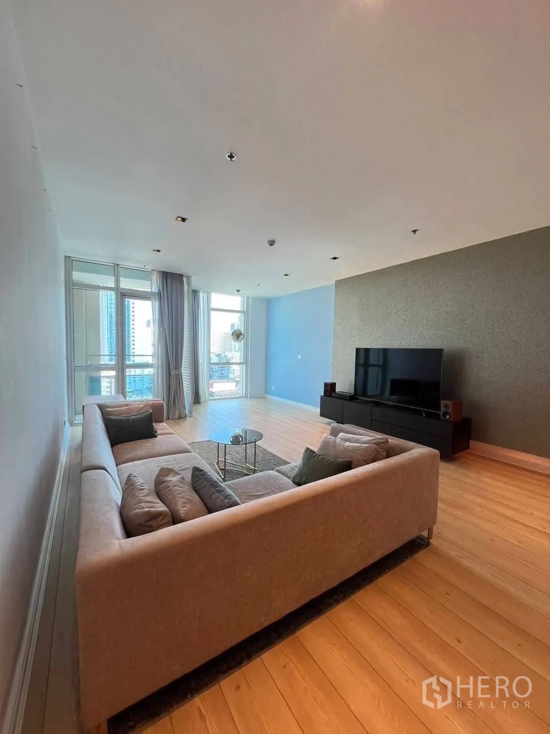 Condominium for rent in Pathum Wan, Bangkok - Spacious living room with sectional sofa, TV console, and large windows.