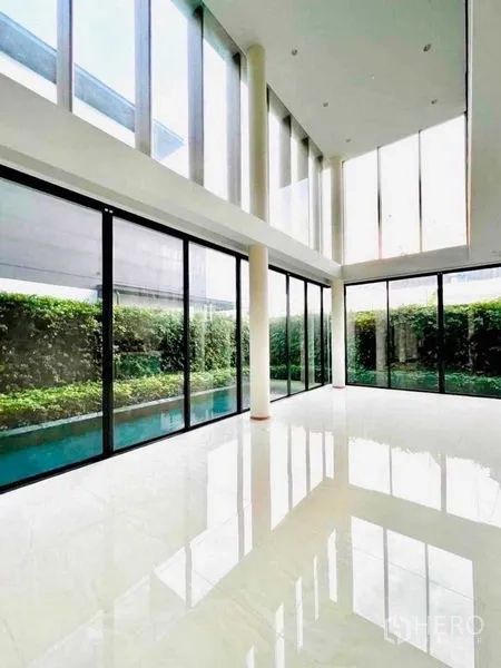 Detached House for sale in Huai Khwang, Bangkok - Sunlit double-height lounge with tall windows looking onto the pool and garden.