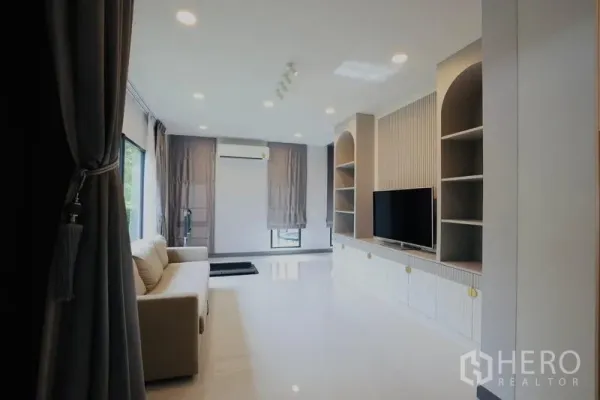 Detached House for rent in Bang Phli, Samut Prakan - Spacious family room with built-in TV wall, open shelving, and grey curtains.