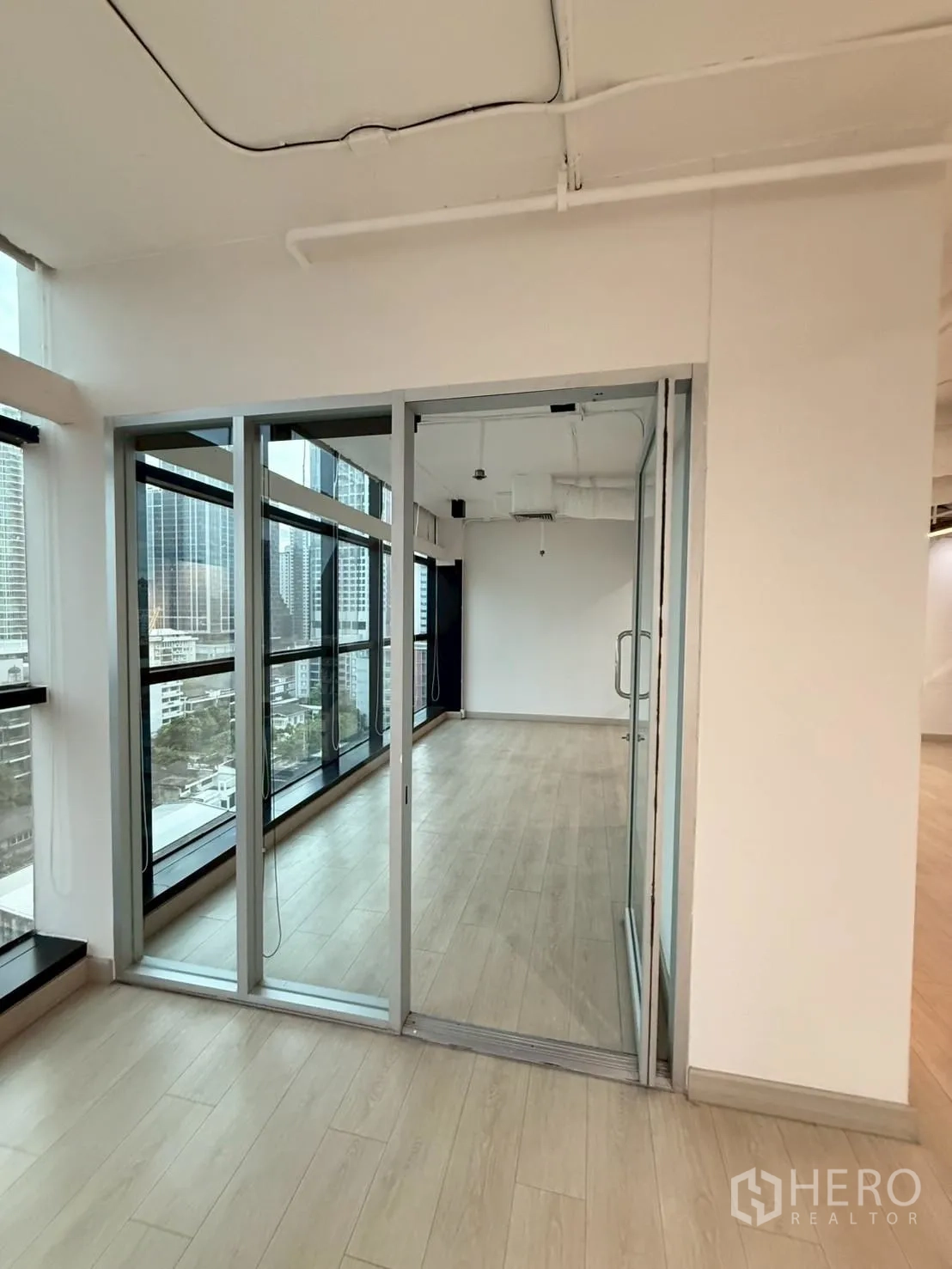 Office Space for rent in Watthana, Bangkok - Glass-partitioned room beside floor-to-ceiling windows and wood-look floors.