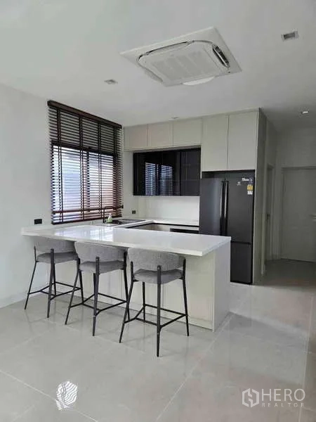 独立式住宅 出租在Bang Phli, Samut Prakan - 明亮厨房，中岛吧台、吊柜与黑色冰箱。