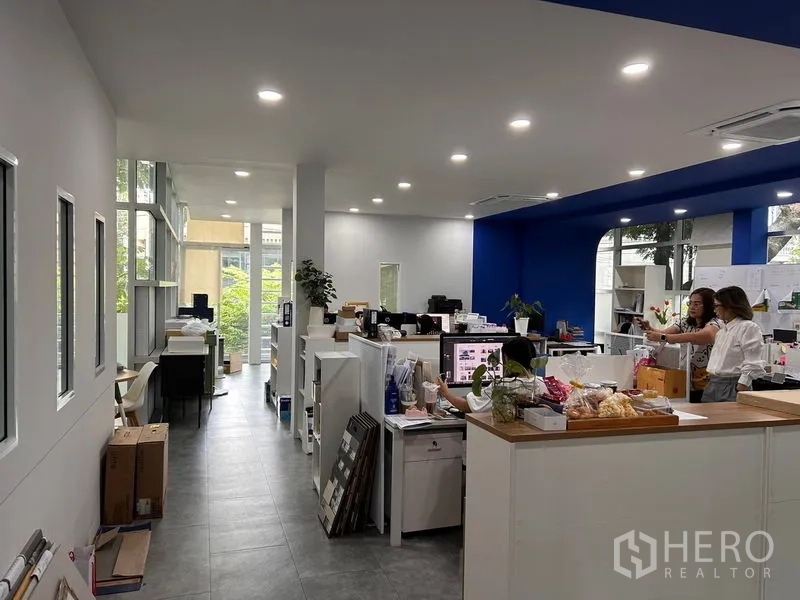 Office Space for rent in Khlong Toei, Bangkok - Bright open‑plan workspace with recessed lighting, white workstations and a bold blue accent wall beside tall windows.
