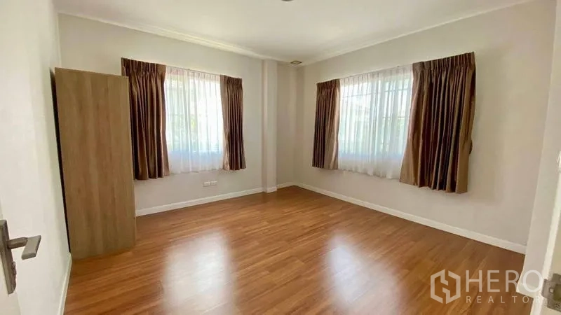 Detached House for rent in Bang Kapi, Bangkok - Guest bedroom with wood flooring and two windows with curtains.