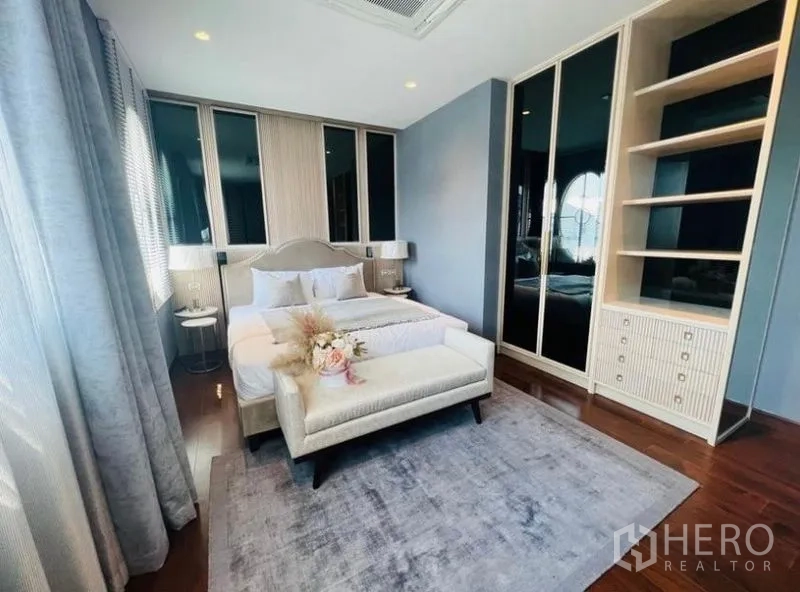 Detached House for rent or sale in Watthana, Bangkok - Bedroom with large windows, upholstered bed, built-in wardrobes and bench.