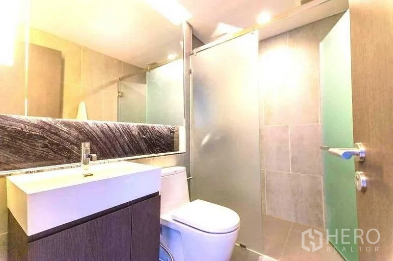 Condominium for rent in Khlong Toei, Bangkok - Modern bathroom with vanity, toilet and frosted glass shower enclosure.