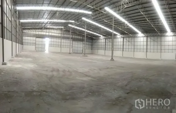 Warehouse for rent in Bang Phli, Samut Prakan - Wide-angle view of warehouse interior with central columns, skylights and a large roller shutter door.