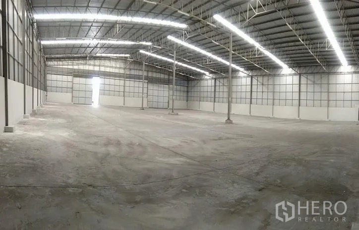 Warehouse for rent in Bang Phli, Samut Prakan - Wide-angle view of warehouse interior with central columns, skylights and a large roller shutter door.