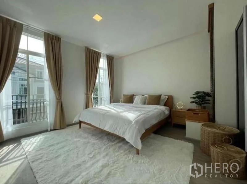 Townhouse for rent in Prawet, Bangkok - Master bedroom with large windows, curtains, and a soft area rug