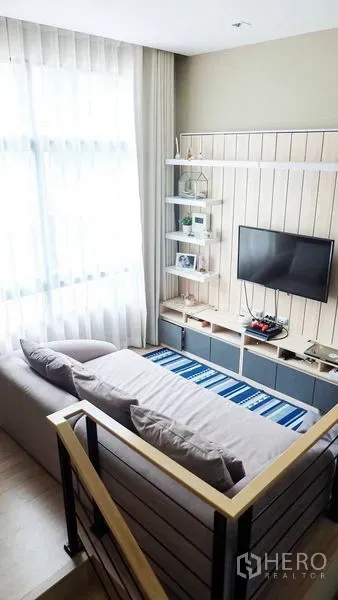 Townhouse for rent or sale in Suan Luang, Bangkok - Cozy TV lounge with sofa, striped rug and built-in media shelves beside the staircase.