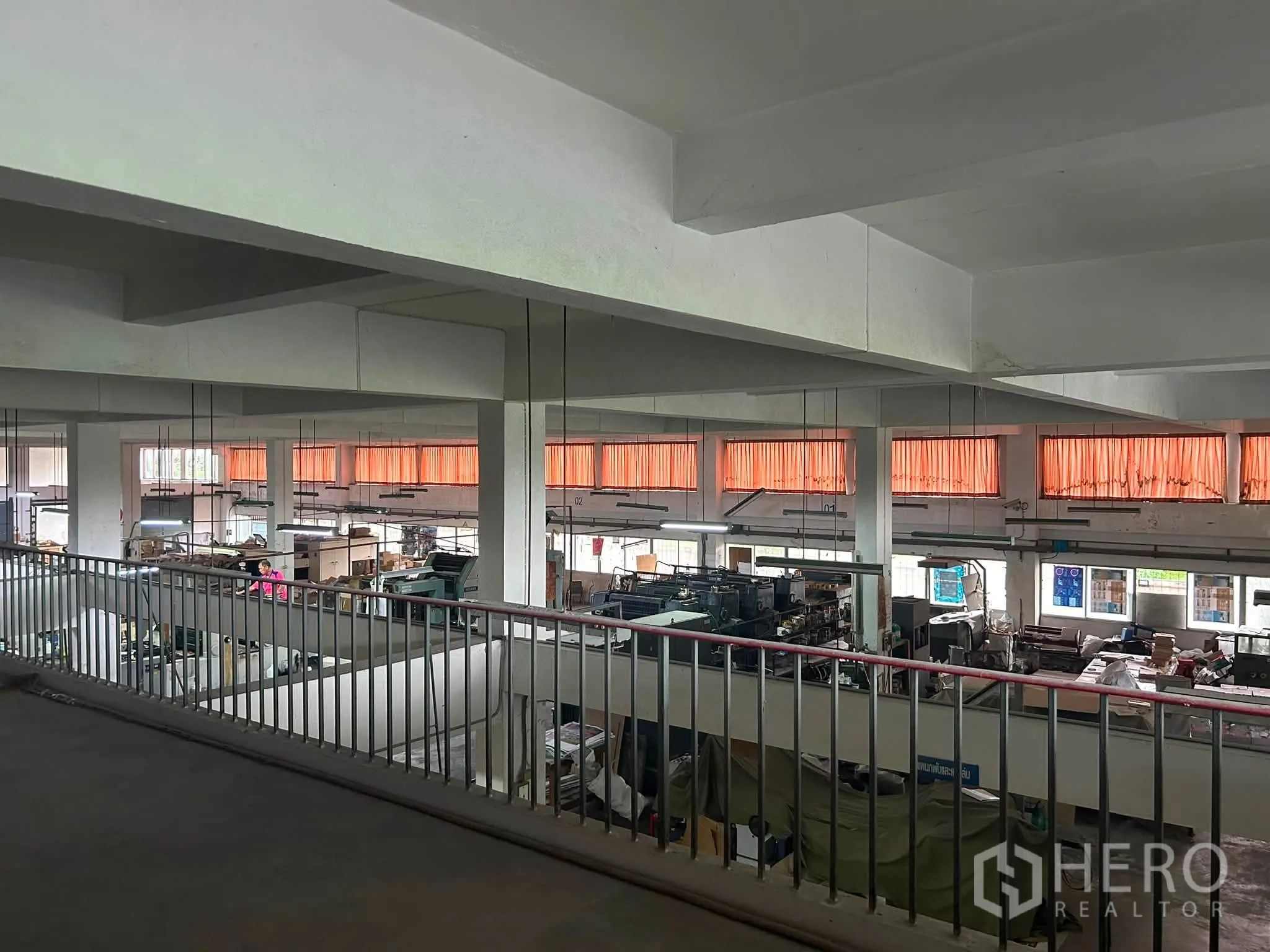 Warehouse for rent in Phra Khanong, Bangkok - Mezzanine walkway overlooking a large warehouse floor with columns, windows, and hanging lights.