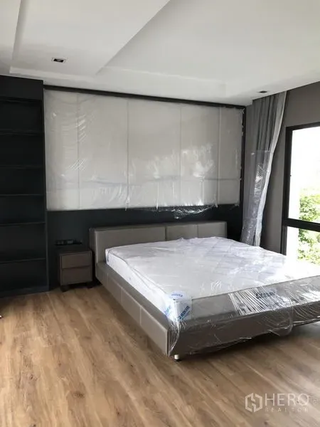 Detached House for rent in Bang Kapi, Bangkok - Primary bedroom with wood flooring, large windows and upholstered headboard wall.
