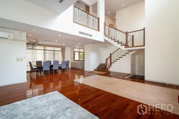 Detached House for rent in Watthana, Bangkok - Double-height living and dining area with hardwood floors and a feature staircase in a detached house in Watthana, Bangkok.